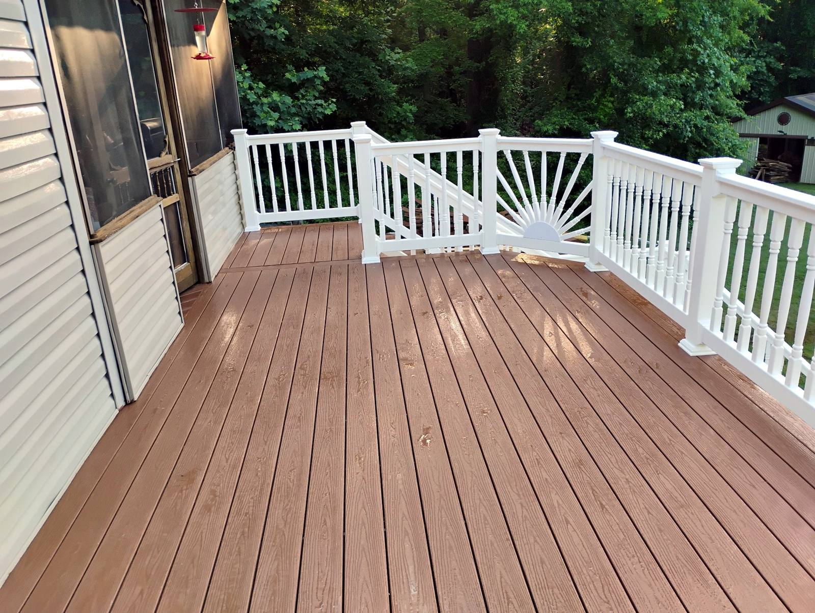 Finished brown deck and white railing beside a home