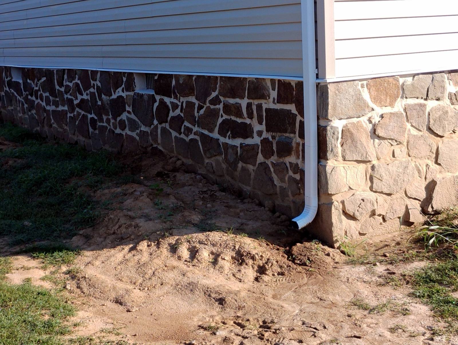 Stone foundation and downspout detail beside a finished home